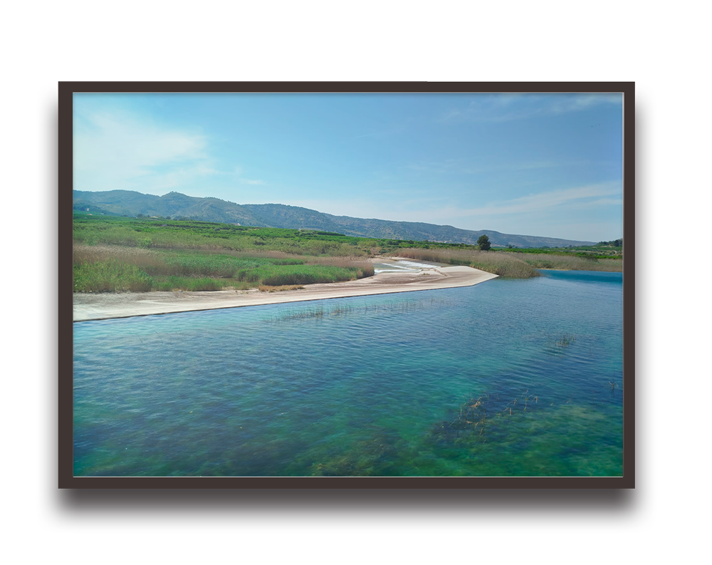 Framed landscape photo of a calm river winding through grassy wetlands toward distant hills under a blue sky.