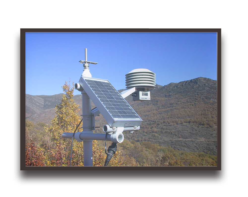 Solar-powered environmental monitoring station with a solar panel and sensor on a pole in a mountainous landscape.