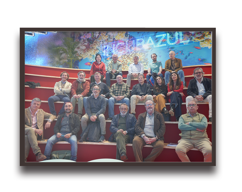Group of about twenty adults seated on red steps in front of an underwater mural.