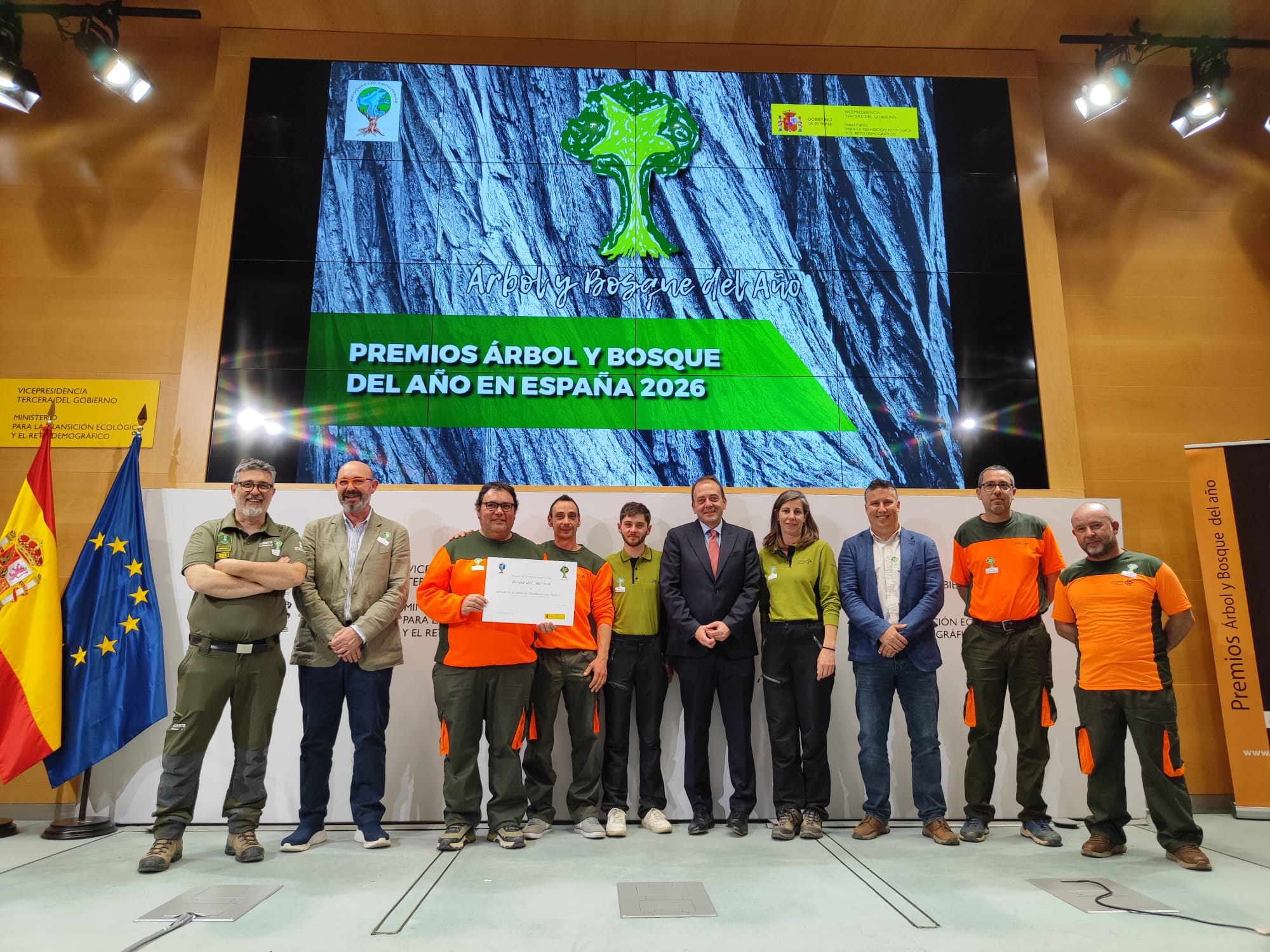 Group of award recipients on stage at a ceremony for Árbol y Bosque del Año en España 2026, with Spanish and EU flags and a large screen banner in the background.