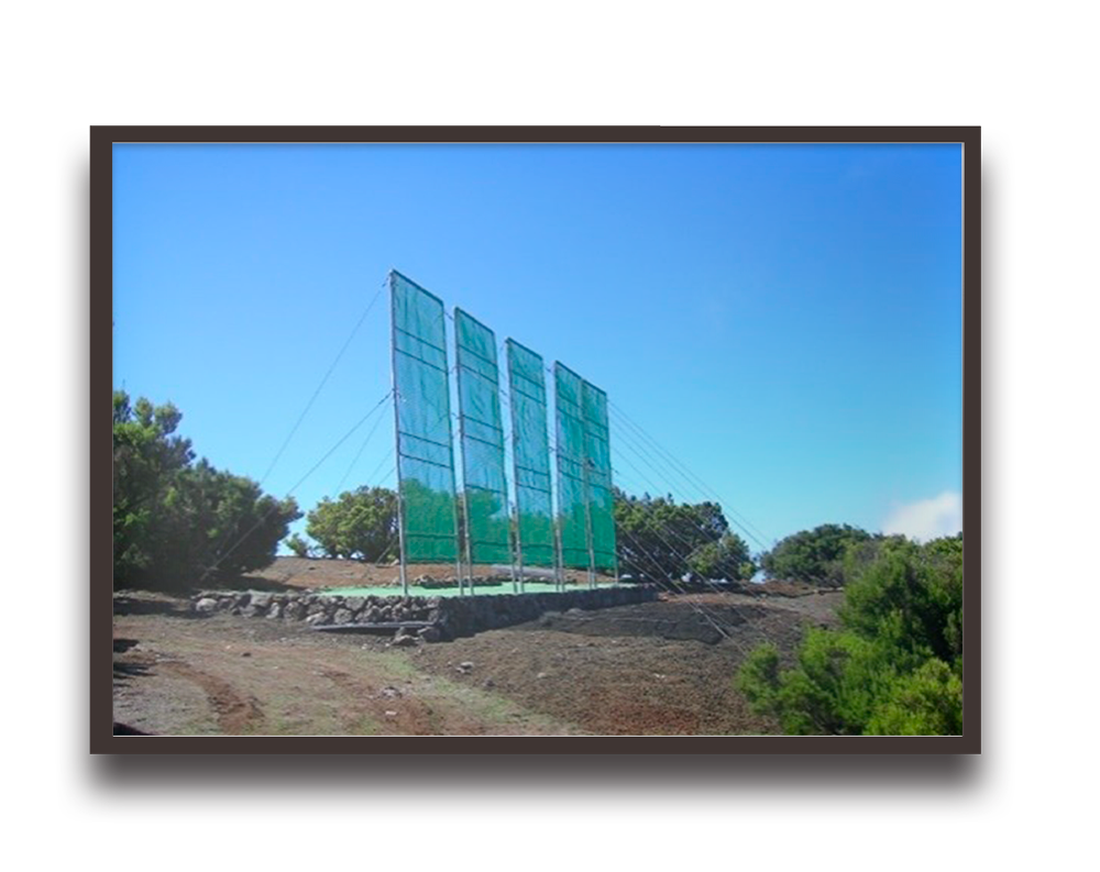 Three tall green panels mounted on a hillside, supported by cables against a blue sky.