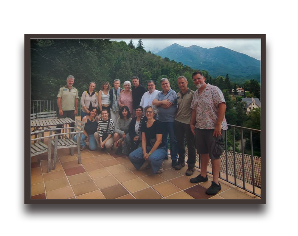 Group of adults posing together on a tiled terrace with mountains and trees in the background.