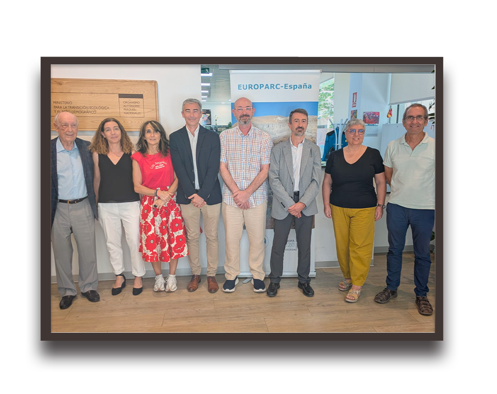Group of eight adults standing in a row at an exhibition booth with a EUROPARC-España banner behind them.
