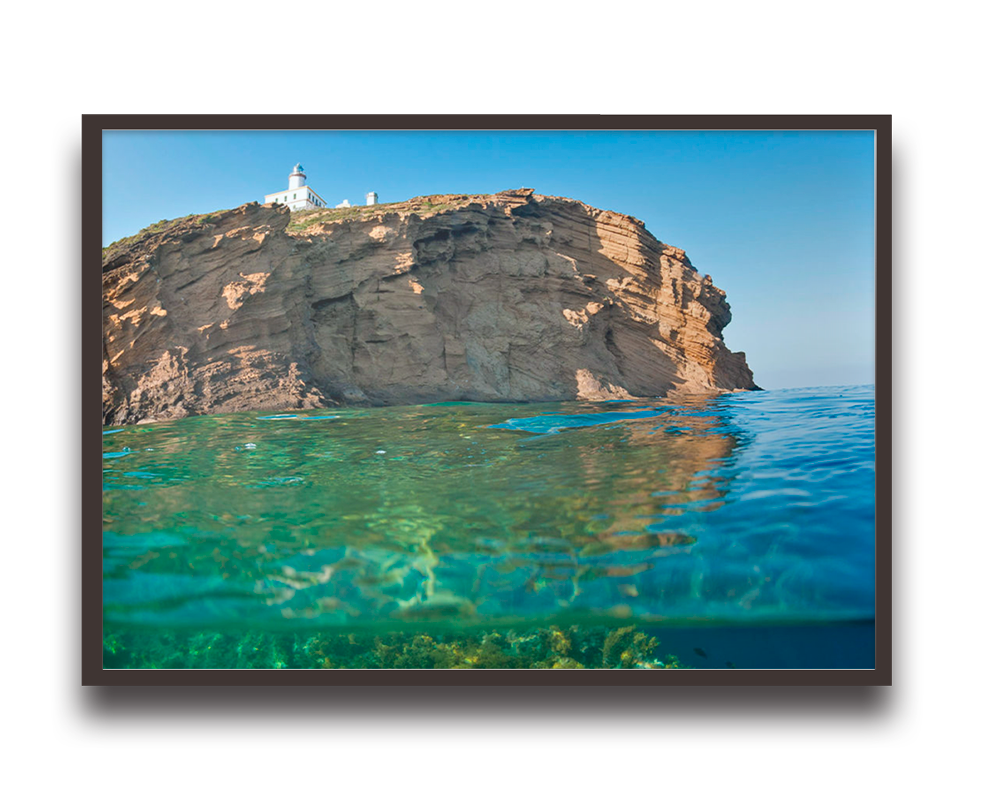 A rocky cliff with a lighthouse on top overlooking clear turquoise water, shown in a split underwater/above-water view within a framed photo.