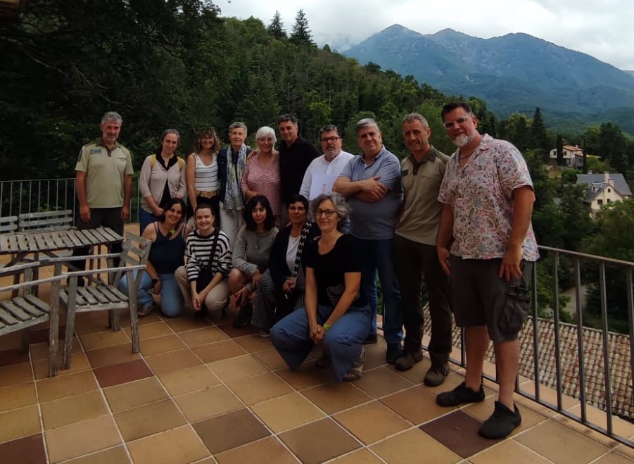 Group of about 14 adults posing together on a tiled terrace with trees and mountain peaks in the background.