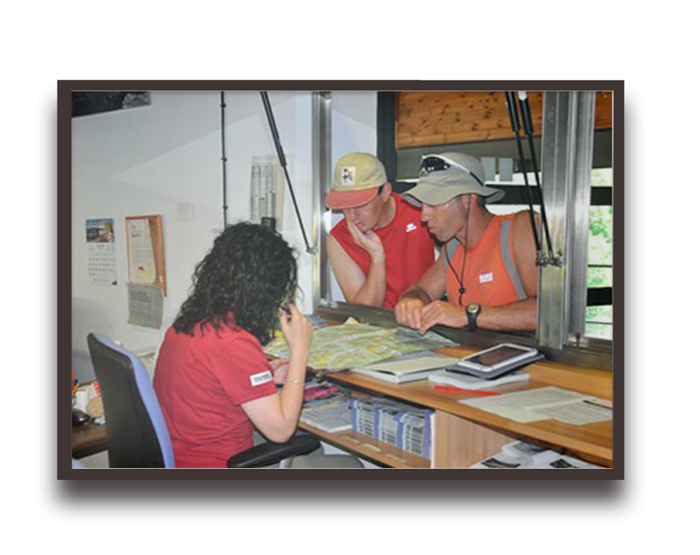 Three people study a large map at a desk, indoors, planning or coordinating a field task.